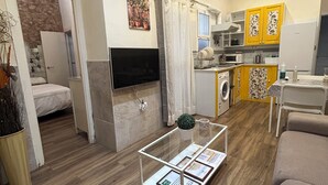 Een moderne woonkamer met een flatscreen televisie, een glazen salontafel met documenten, een bank en een eethoek met gele kasten.