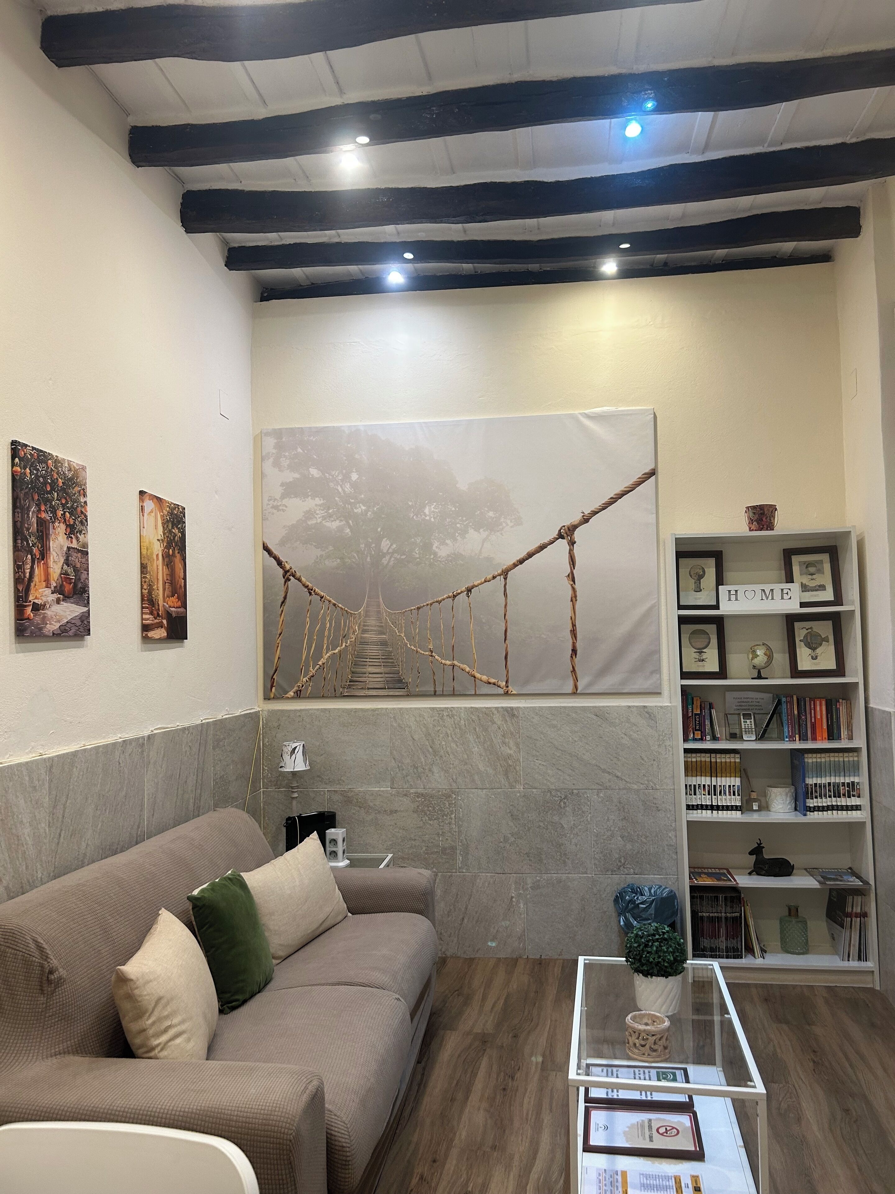 A modern living room with a sofa, a coffee table, a bookshelf, and a large painting of a tree.