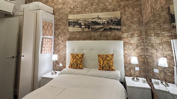 Een slaapkamer met een stenen muur, een bed met wit beddengoed, twee nachtkastjes met lampen en een grote spiegel.