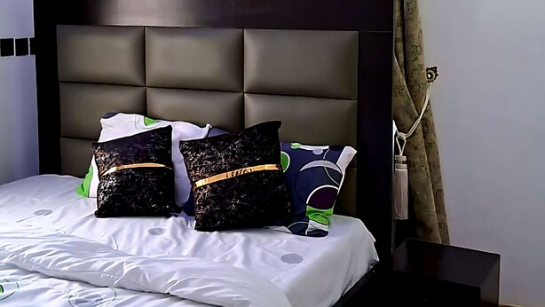 A modern bedroom with a large bed, a headboard, and a nightstand.