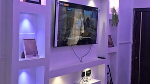 A modern living room with a flat-screen TV mounted on a white wall, surrounded by built-in shelves and recessed lighting.
