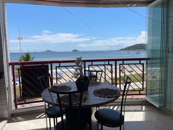 A balcony with a table and chairs, overlooking a beach and ocean.