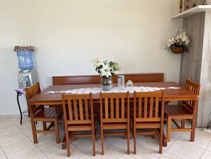 A dining table with six wooden chairs, a water dispenser, a vase with flowers, and a lace tablecloth.