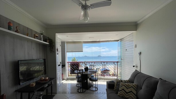 A living room with a TV, sofa, and dining area with a view of the sea. - Cozy beachfront apartment in Enseada, ideal for families and groups. (São Francisco do Sul)
