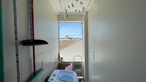 A laundry room with a washing machine, drying rack, and ironing board. - Cozy beachfront apartment in Enseada, ideal for families and groups. (São Francisco do Sul)
