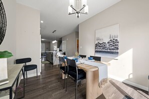 A modern kitchen with a central island, a dining area with a wooden table and chairs, and a large painting on the wall. - Large Home | Sleeps 12 | Yard | Near DT & Stadium (Edmonton)