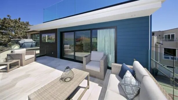 Un edificio moderno con techo plano, grandes ventanales y un patio con mobiliario exterior.