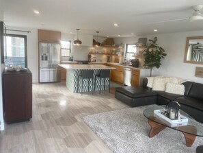 Eine moderne Küche mit einer zentralen Kochinsel, eine Essecke mit einer Couch und ein Wohnzimmer mit Couchtisch.