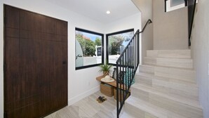 Un interior moderno con una puerta de madera oscura, una escalera con barandillas negras y vistas a través de un ventanal grande.