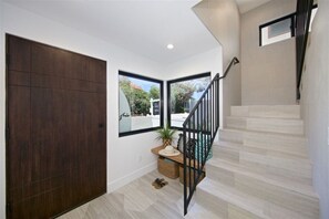 Ein modernes Interieur mit einer dunklen Holztür, einer Treppe mit schwarzen Geländern und einem Ausblick durch ein großes Fenster.