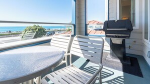 A balcony with a table and chairs, a grill, and a view of the ocean.