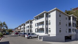 A multi-story residential building with balconies, a parking area, and a clear sky.