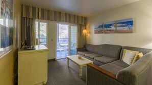 A hotel room with a sofa, a small table, a lamp, and a view of the outdoors through a sliding door.