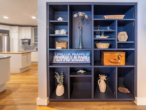 Una cocina con armarios blancos, encimera de madera y una unidad de estanterías azules con objetos decorativos.