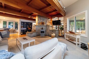A spacious living area with a stone fireplace, wooden beams, a television, and a view of the outdoors.