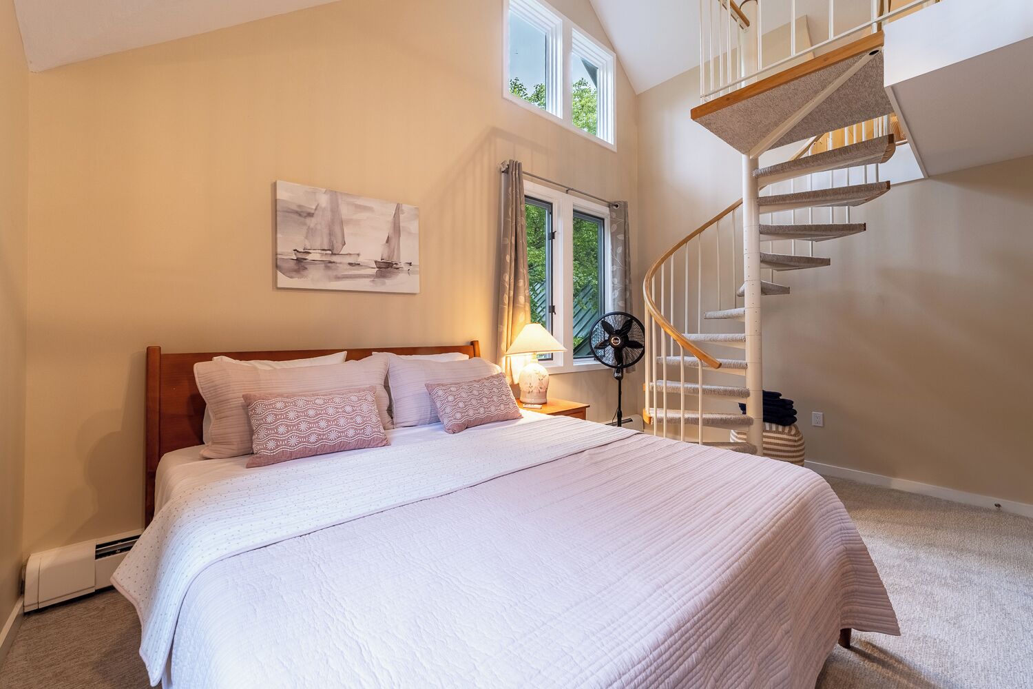 A bedroom with a bed, a nightstand, a fan, a window, and a spiral staircase.