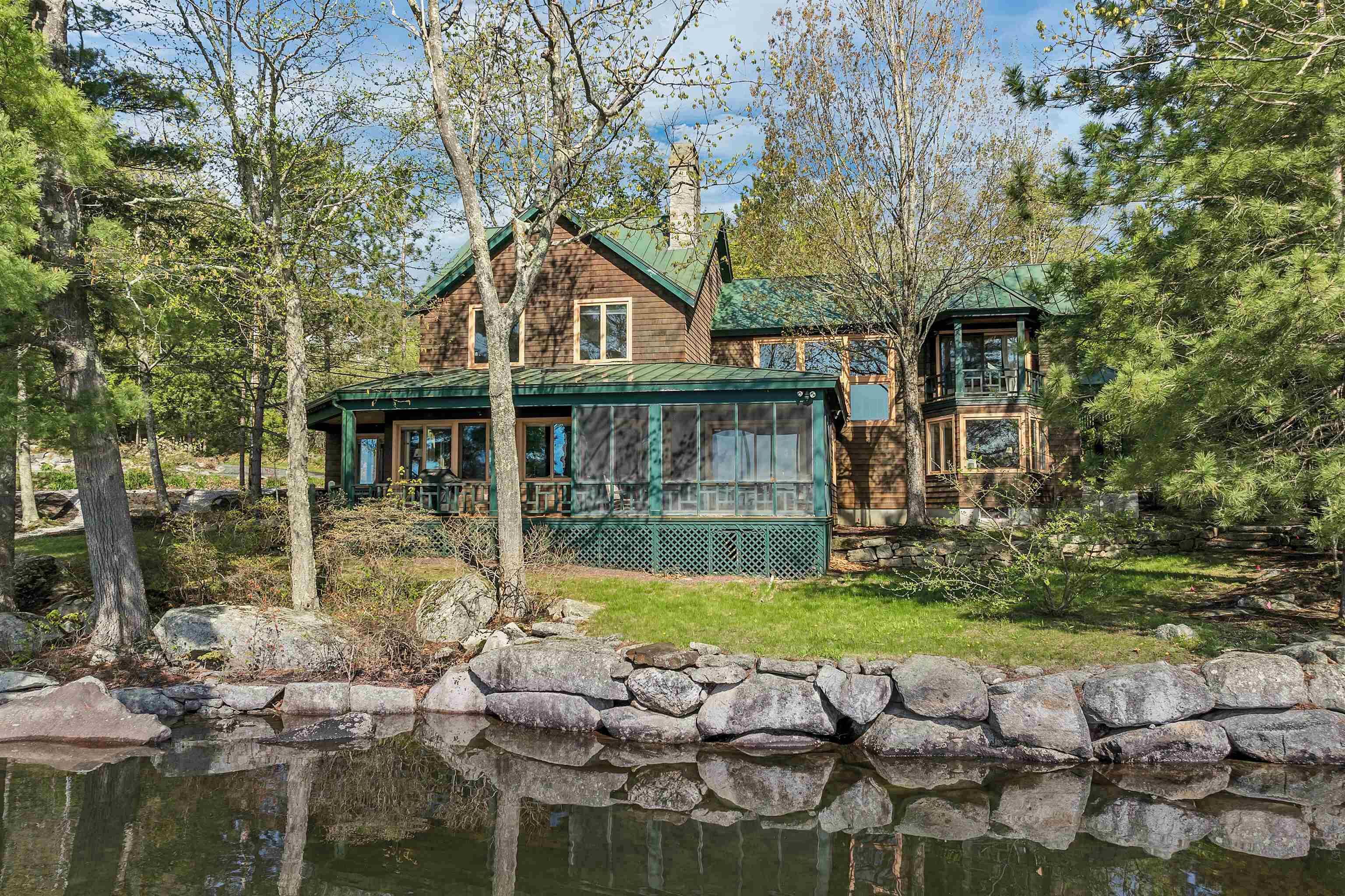 A cabin with a green roof, surrounded by trees and a pond.