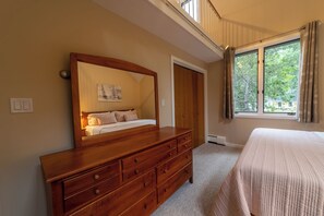 Un dormitorio con un gran aparador de madera, una cama con manta texturizada, una ventana con cortinas y una puerta que da a otra habitación.