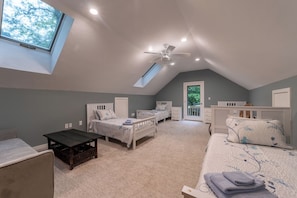 A bedroom with two beds, a ceiling fan, a skylight, and a door leading to an outdoor area.