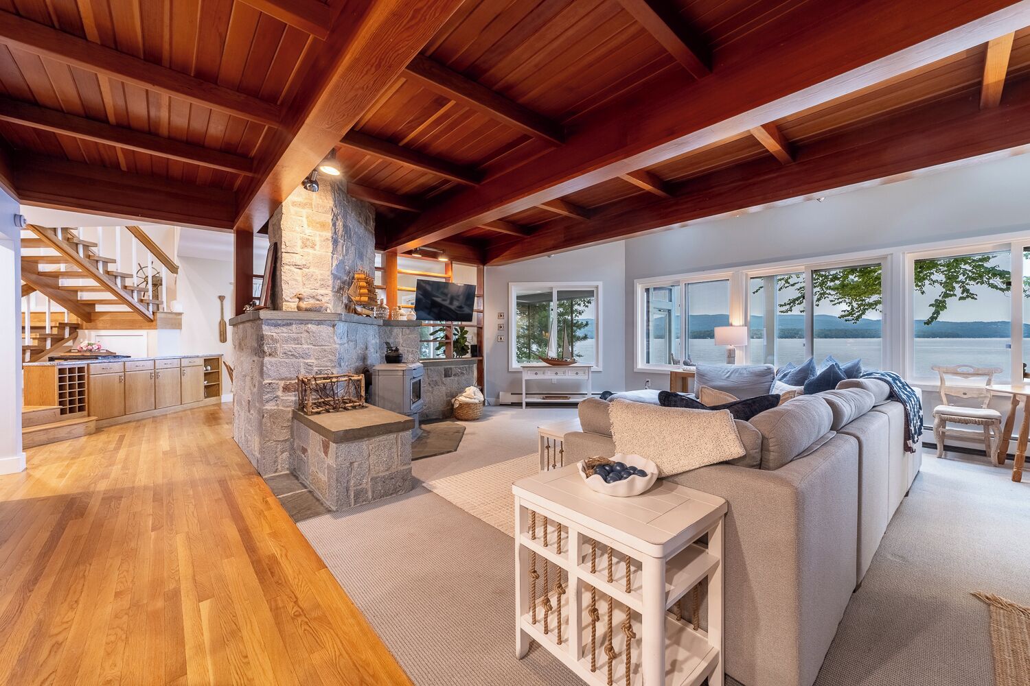 A spacious living area with a stone fireplace, wooden beams, a sofa, and a view of the lake.