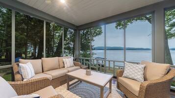 A covered outdoor seating area with a sofa, chairs, and a table, overlooking a body of water.