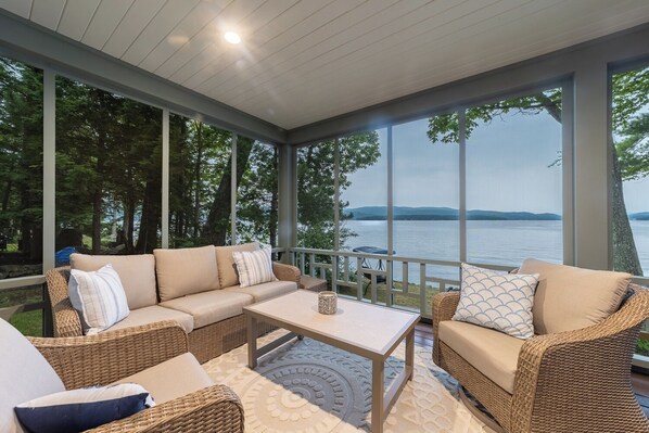 A covered outdoor seating area with a sofa, chairs, and a table, overlooking a body of water.