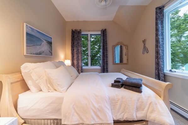 A bedroom with a bed, a window, a painting, and a mirror.