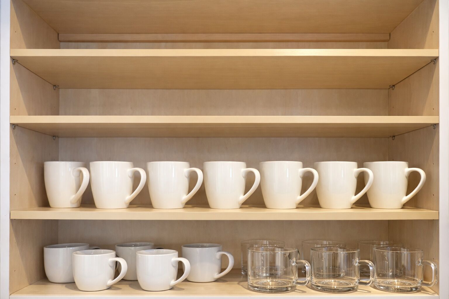 Una estantería de madera con tazas blancas y de vidrio transparente.