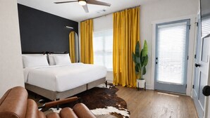 Un dormitorio con cama, ventilador de techo, planta en maceta, puerta y sillón de cuero marrón.