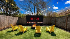 Patio trasero con pantalla de Netflix, asientos exteriores y un brasero.