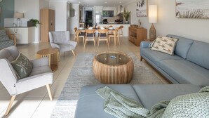 Ein modernes Wohnzimmer mit einer Couch, Sesseln, einem Couchtisch und einem Essbereich mit Stühlen und einem Tisch.