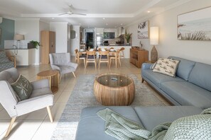 A modern living room with a sofa, armchairs, a coffee table, and a dining area with chairs and a table. - Blue Water Views 3 & Free Buggy- Hamilton Island (Hamilton Island)