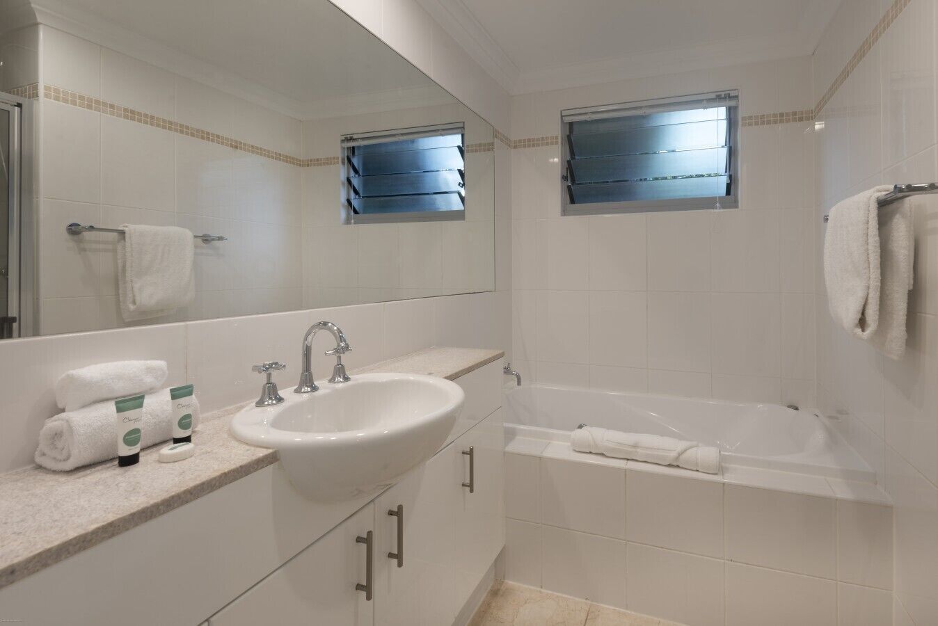 Une salle de bain avec un lavabo, un miroir, une fenêtre et une baignoire.