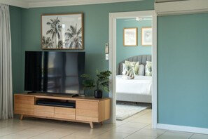 Een kamer met een televisie op een houten kast, een plant en een bed met kussens.