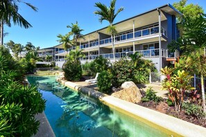 A hotel with a swimming pool, surrounded by tropical plants and palm trees. - Blue Water Views 3 & Free Buggy- Hamilton Island (Hamilton Island)