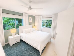 A bedroom with a bed, nightstand, lamp, ceiling fan, and large windows with curtains. - Blue Water Views 3 & Free Buggy- Hamilton Island (Hamilton Island)