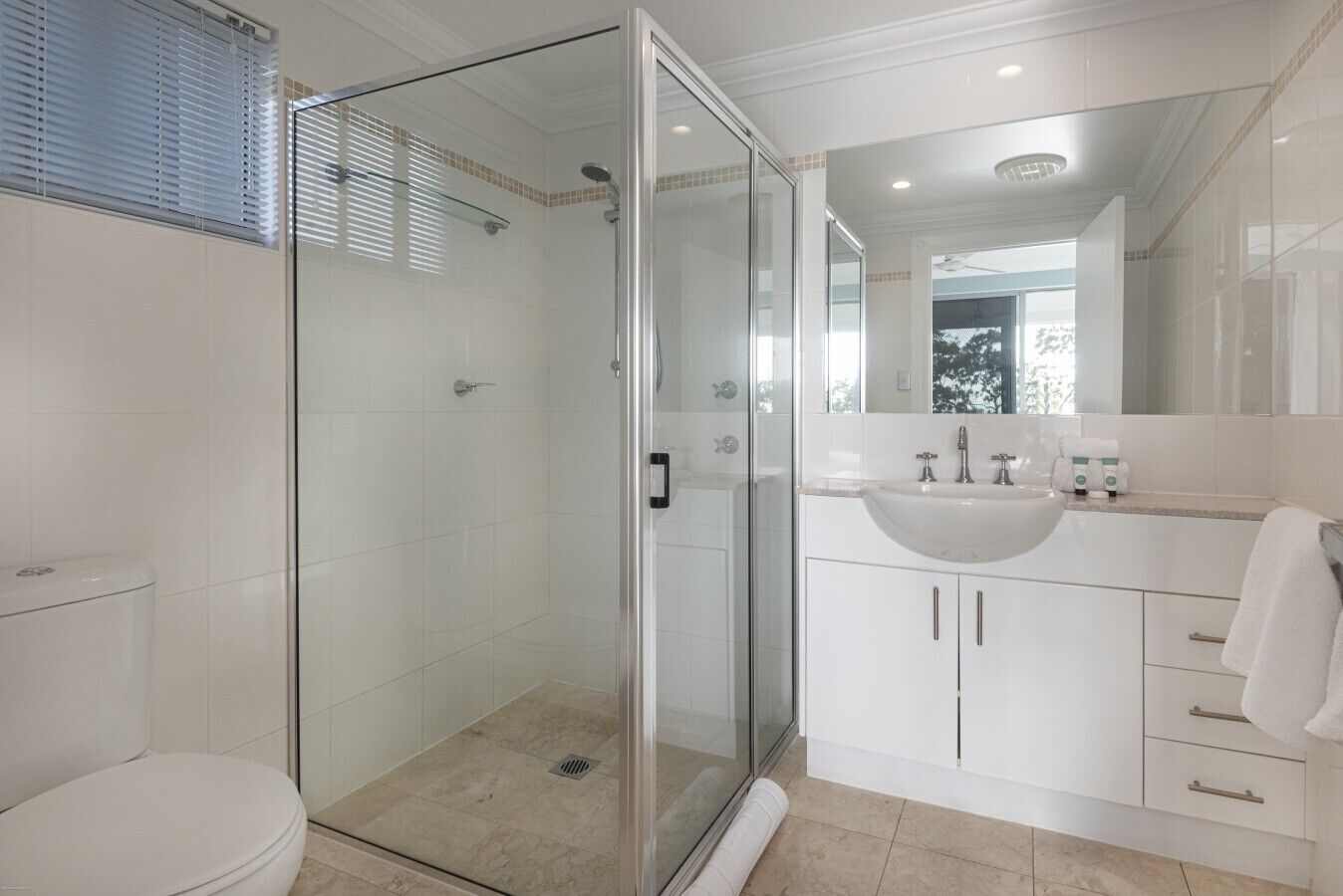Un bany modern amb dutxa envidriada, un lavabo blanc i un mirall gran.