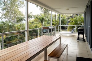 A balcony with a wooden bench, a grill, and a view of tropical vegetation. - Blue Water Views 3 & Free Buggy- Hamilton Island (Hamilton Island)