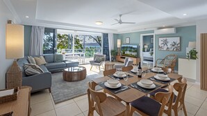Ein modernes Wohnzimmer mit Sofa, Esstisch und Stühlen, ein Balkon mit Aussicht sowie ein Fernseher.