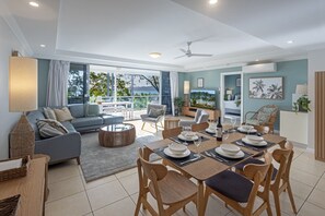 A modern living room with a sofa, dining table, and chairs, a balcony with a view, and a television. - Blue Water Views 3 & Free Buggy- Hamilton Island (Hamilton Island)