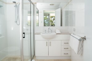 A modern bathroom with a glass shower enclosure, a white sink, and a large mirror. - Blue Water Views 3 & Free Buggy- Hamilton Island (Hamilton Island)