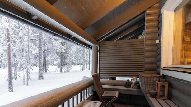 Eine Holzhütte mit einer Bank und einem Tisch neben einem Fenster mit Blick auf einen verschneiten Wald.
