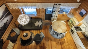 Ein gemütliches Blockhaus-Interieur mit Holzboden, einer Couch, einem Esstisch und einer Küchenzeile.