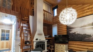 Ein Holzblockhaus-Innenraum mit Kamin, Holzwänden, einem Fernseher und einer Leiter.
