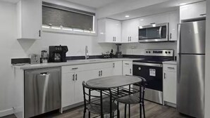 A modern kitchen with stainless steel appliances, white cabinetry, and a central island with stools. - Oshmild Suites, 5 mins to various shops and Cinema (Saskatoon)