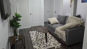 A living room with a grey sofa, white cushions, a small side table, a potted plant, and a patterned rug. - Oshmild Suites, 5 mins to various shops and Cinema (Saskatoon)