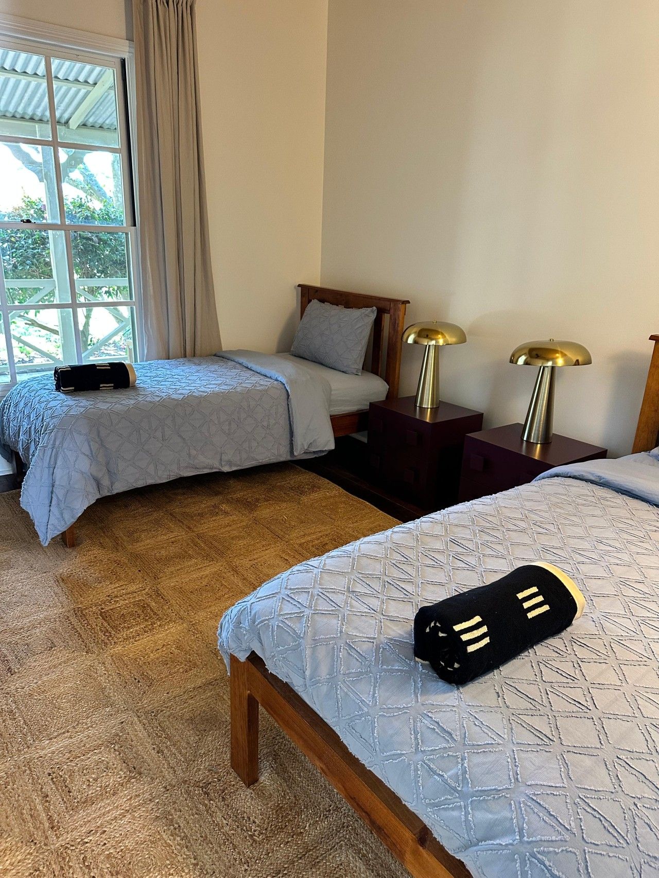 Una camera d'albergo con due letti, un'ampia finestra con tende e due abat-jour.