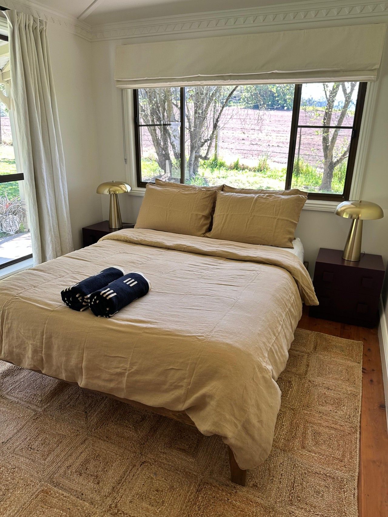 A bedroom with a bed, two bedside tables, a window with curtains, and a view of the outdoors.