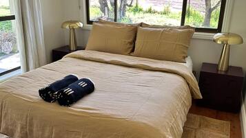 A bedroom with a bed, two bedside tables, a window with curtains, and a view of the outdoors.