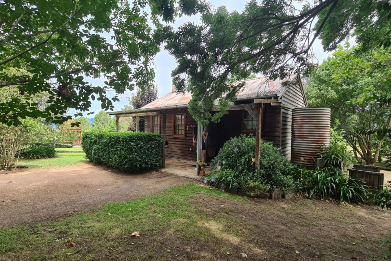A rustic wooden building with a porch, surrounded by lush greenery and a well-maintained garden.